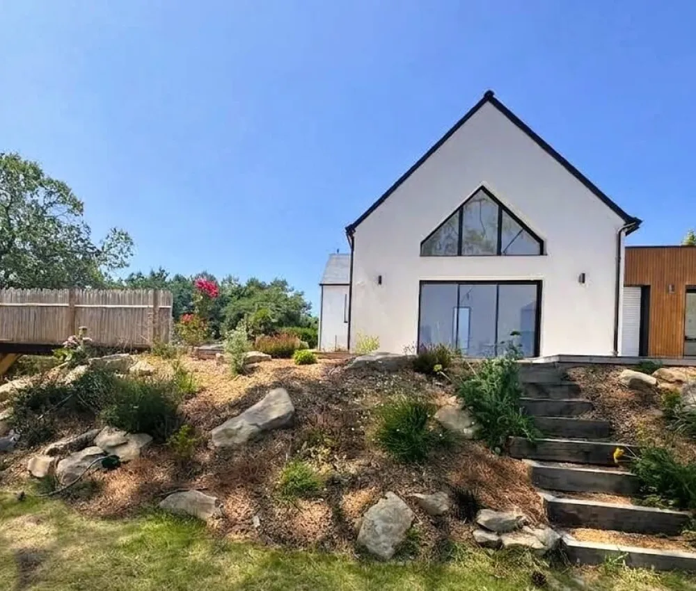 maison blanche moderne avec toit pointu et escalier en bois sur un terrain en pente