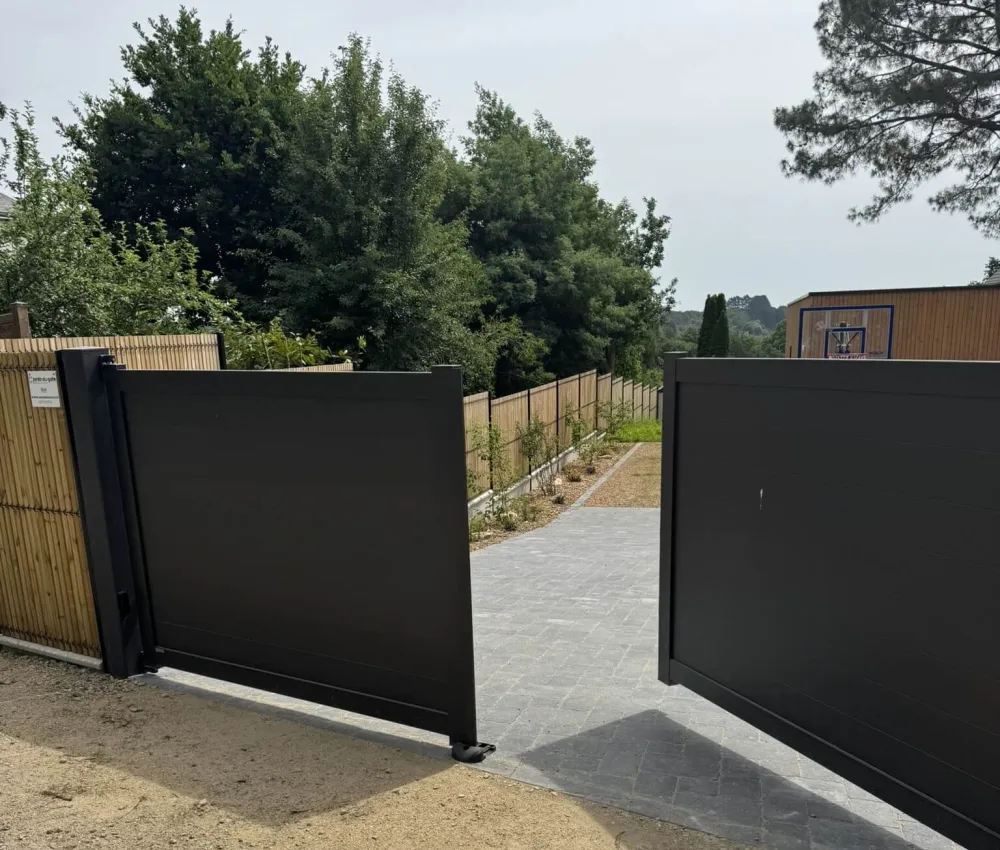 portail en aluminium noir avec allée pavée menant à un terrain de basket-ball